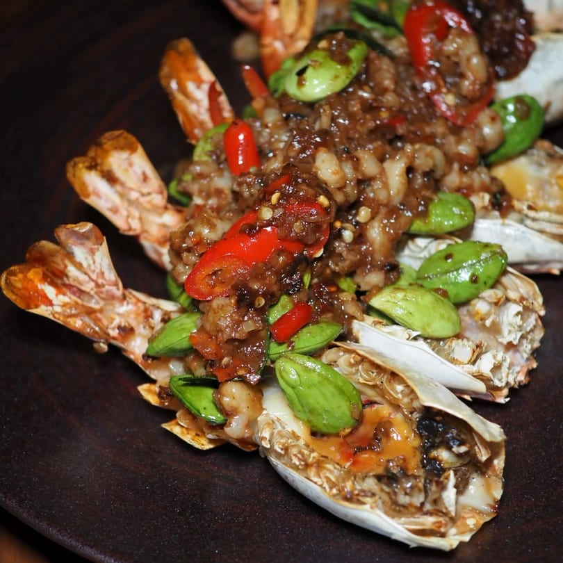 Thai stir-fried shrimp with red chilies and green beans on a dark plate.