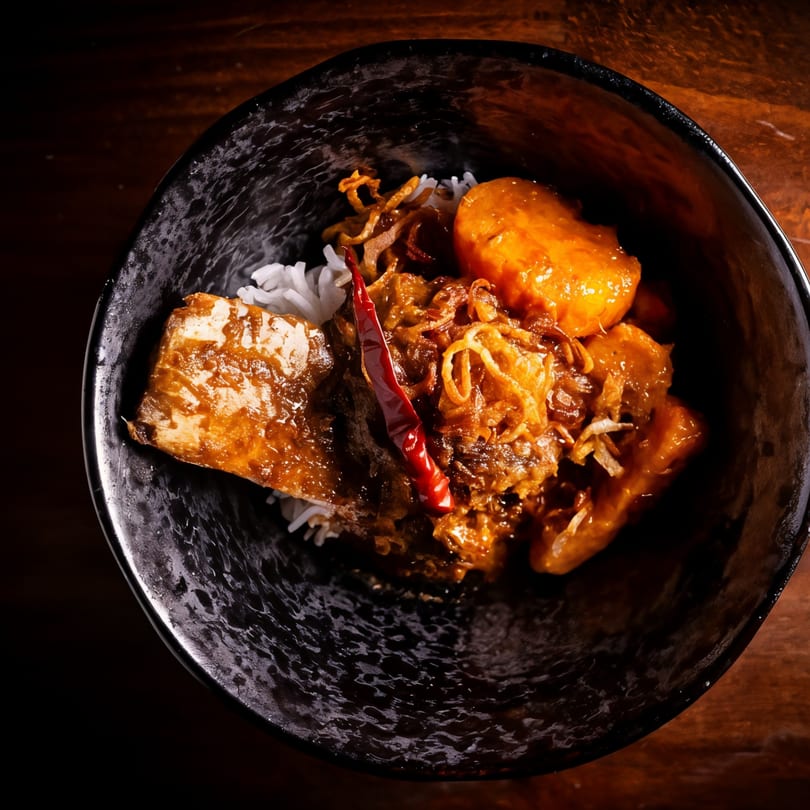 Chao Krung Thai's Massaman Curry with fish, potatoes, and rice in a dark bowl.